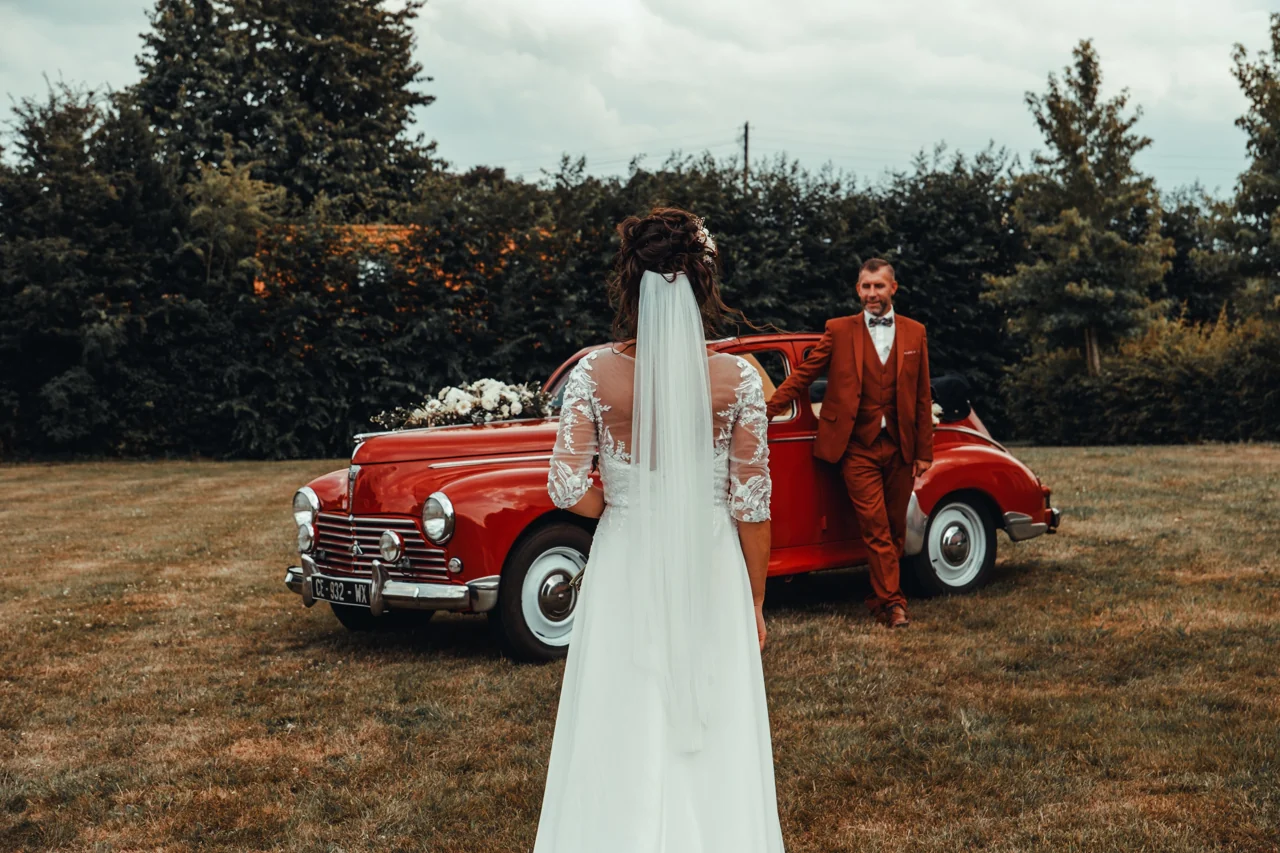 La mariée retrouve son époux devant une voiture ancienne rouge